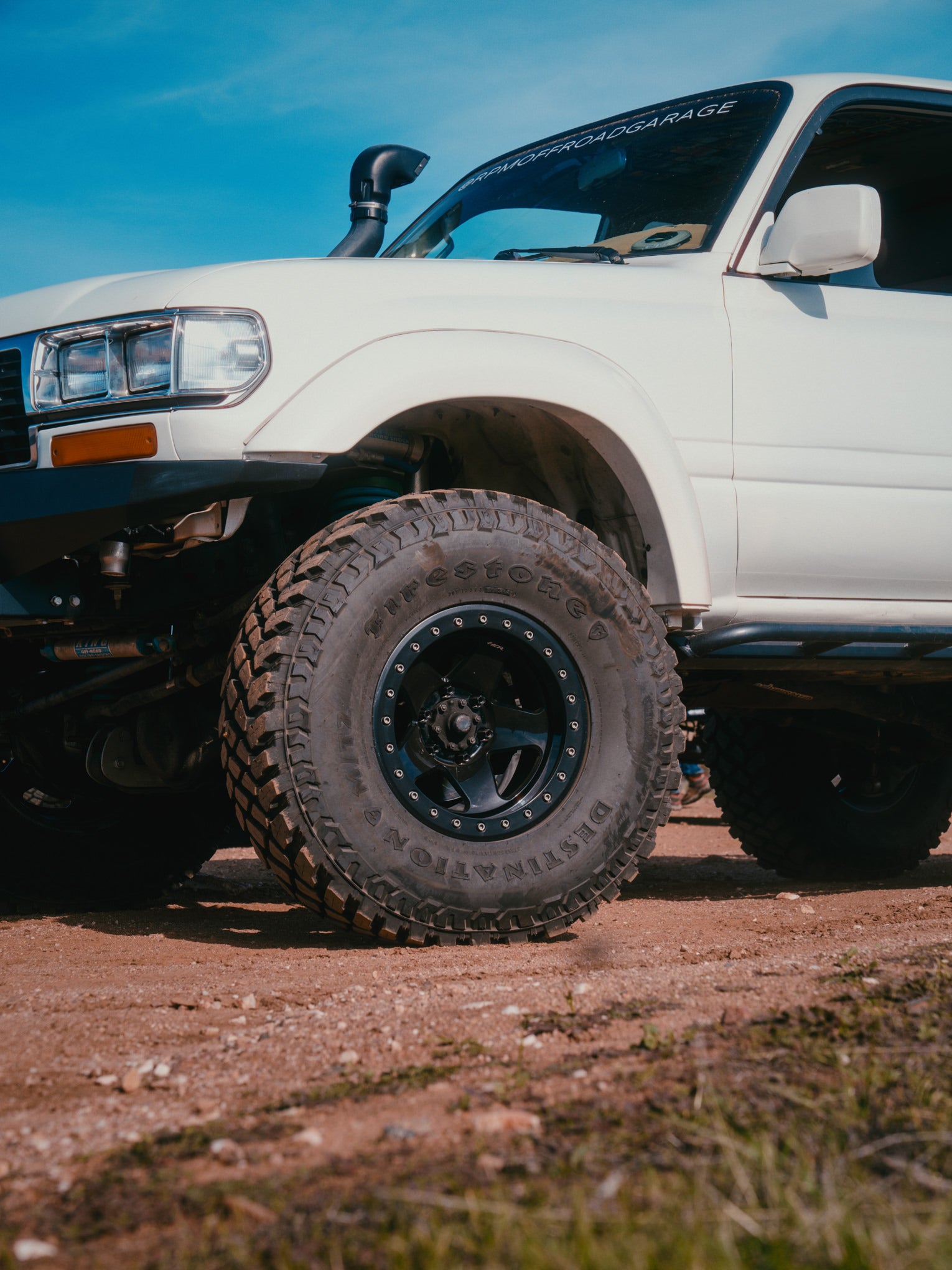 White truck with large off-road tires and forged wheels on a dirt road